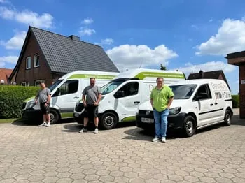 Drei Männer stehen vor drei weißen Lieferwagen mit grünen und schwarzen Logos.
